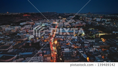 Malta, Comino island: Cars driving on illuminated urban traffic night road, showcasing vibrant cityscape streets lights and buildings with traditional and modern architecture. Drone flight Malta, Comino island: Cars driving on illuminated urban traffic night road, showcasing vibrant cityscape streets lights and buildings with traditional and modern architecture. Drone flight 139489142