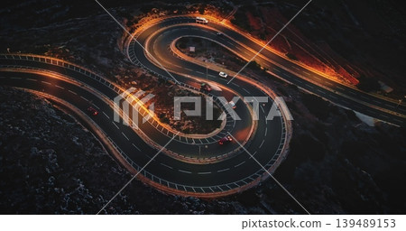Malta: Night traffic. Cars driving on a winding road at sunset illuminating the Maltese landscape with orange street lights, creating a mesmerizing aerial view. Static shot Malta: Night traffic. Cars driving on a winding road at sunset illuminating the Maltese landscape with orange street lights, creating a mesmerizing aerial view. Static shot 139489153
