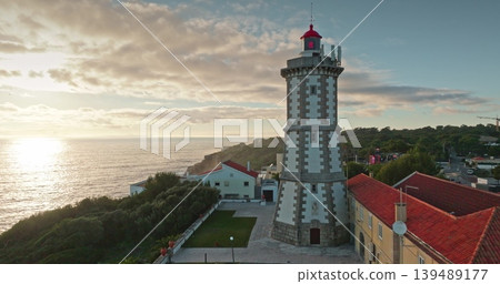 Portugal, Lisbon: Aerial view of Santa Marta Lighthouse at sunset, overlooking the town of Cascais and coastline, a beacon of light guiding ships along the Atlantic coast. Drone 139489177