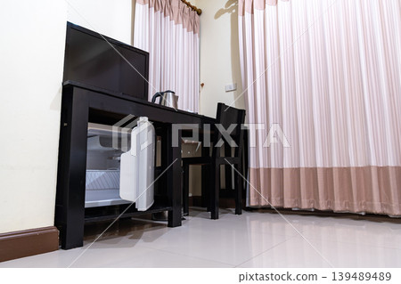 A small refrigerator sits beneath a wooden desk with chair, creating a clean hotel room setup that supports minibar service and compact guest comfort. A small refrigerator sits beneath a wooden desk with chair, creating a clean hotel room setup that supports minibar service and compact guest comfort. 139489489