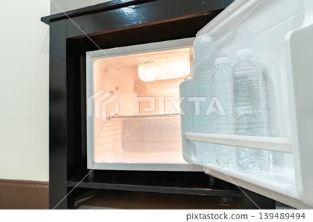 A small refrigerator sits beneath a wooden desk with chair, creating a clean hotel room setup that supports minibar service and compact guest comfort. A small refrigerator sits beneath a wooden desk with chair, creating a clean hotel room setup that supports minibar service and compact guest comfort. 139489494