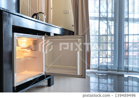 A small refrigerator sits beneath a wooden desk with chair, creating a clean hotel room setup that supports minibar service and compact guest comfort. A small refrigerator sits beneath a wooden desk with chair, creating a clean hotel room setup that supports minibar service and compact guest comfort. 139489496