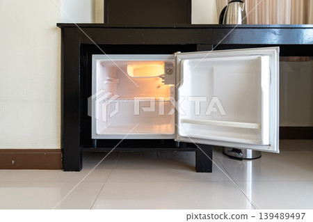A small refrigerator sits beneath a wooden desk with chair, creating a clean hotel room setup that supports minibar service and compact guest comfort. A small refrigerator sits beneath a wooden desk with chair, creating a clean hotel room setup that supports minibar service and compact guest comfort. 139489497