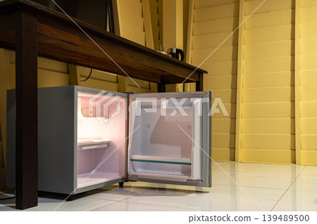 A small refrigerator sits beneath a wooden desk with chair, creating a clean hotel room setup that supports minibar service and compact guest comfort. A small refrigerator sits beneath a wooden desk with chair, creating a clean hotel room setup that supports minibar service and compact guest comfort. 139489500