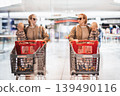 Mother shopping with his kid in the mall. Mother pushing shopping cart while holding and carrying her toddler baby boy child along mall corridor. 139490116