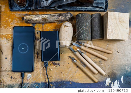 Carpenter's workbench with carving tools and a smartphone charging from a power bank. Carpenter's workbench with carving tools and a smartphone charging from a power bank. 139490713
