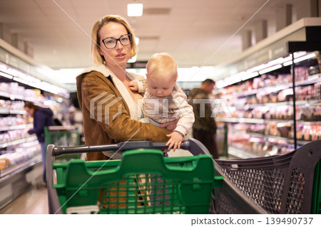 Caucasian mother shopping with her infant baby boy child choosing products in department of supermarket grocery store Caucasian mother shopping with her infant baby boy child choosing products in department of supermarket grocery store 139490737