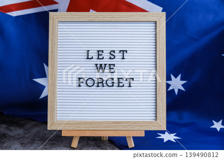 Somber Australian flag backdrop with text LEST WE FORGET on letter board. Respectful message for memorial ANZAC. Concept of remembrance and honor 139490812