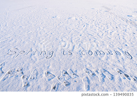 Written SPRING IS COMING on snow background message ice outdoor on ground in winter. Writing text sign and drawing on field in frozen background. Weather is changing cold season has arrived. Mockup 139490835