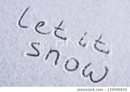 Written LET IT SNOW on snow background message ice outdoor on ground in winter. Writing text sign and drawing on field in frozen background. Weather is changing cold season has arrived. Mockup Copy 139490838