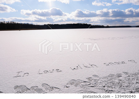Written IN LOVE WITH SNOW on snow background message ice outdoor on ground in winter. Writing text sign and drawing on field in frozen background. Weather is changing cold season has arrived. Mockup 139490840