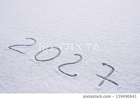 Written sketch for new year 2027. Snow background numbers ice outdoor on ground in winter. Writing text sign and drawing on field in nature frozen background. Copy space 139490841