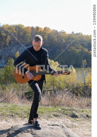 Beautiful blonde man playing acoustic guitar and singing relaxing enjoying outdoors on sunny autumn day. Artist learning and practicing playing musical instrument. Fall leaves autumnal Beautiful blonde man playing acoustic guitar and singing relaxing enjoying outdoors on sunny autumn day. Artist learning and practicing playing musical instrument. Fall leaves autumnal 139490866