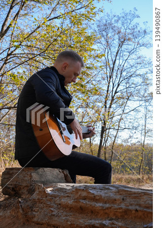 Portrait of smiling caucasian artist plays wooden acoustic guitar in autumnal park. Young songwriter plays string musical instrument hobby outside in nature fall time. Audio music healing 139490867