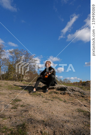 Beautiful blonde man playing acoustic guitar and singing relaxing enjoying outdoors on sunny autumn day. Artist learning and practicing playing musical instrument. Fall leaves autumnal Beautiful blonde man playing acoustic guitar and singing relaxing enjoying outdoors on sunny autumn day. Artist learning and practicing playing musical instrument. Fall leaves autumnal 139490869