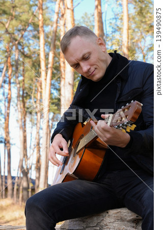 Blonde man playing string guitar outdoors in autumn forest. Concept of sound therapy, mental health and wellness rituals. Calmness tranquility audio-sensory practices. Aura farming energy Blonde man playing string guitar outdoors in autumn forest. Concept of sound therapy, mental health and wellness rituals. Calmness tranquility audio-sensory practices. Aura farming energy 139490875