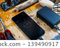 Close-up of a phone screen showing 1% charge, connected to a power bank among wood carving tools and blanks. 139490917
