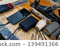 A wide high-angle shot of a phone connected to a 100% charged power bank, surrounded by chisels, wood planes, and logs. 139491366