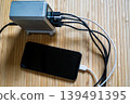 A high-tech silver charging hub with multiple cables connected to a smartphone on a natural bamboo surface. 139491395