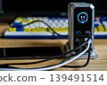 A silver charging hub displaying 11W output, connected to a smartphone and other devices on a desk with a mechanical keyboard. 139491514