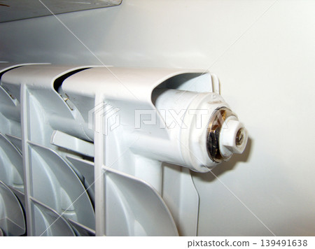 Close-up shot shows a modern white bimetallic radiator section against a plain wall. The focus is on the side plug and air bleed valve, highlighting the clean industrial design and metallic finish Close-up shot shows a modern white bimetallic radiator section against a plain wall. The focus is on the side plug and air bleed valve, highlighting the clean industrial design and metallic finish 139491638