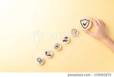 Work safety compliance and risk management concept, hand placing shield check icon above wooden symbols for protection, audit, health care, warning, training, quality control, and workplace safety. Work safety compliance and risk management concept, hand placing shield check icon above wooden symbols for protection, audit, health care, warning, training, quality control, and workplace safety. 139491675