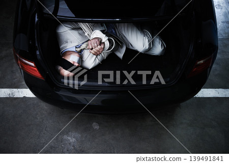 Man in trunk of car, kidnap and rope with danger, violence and fear in basement garage from above. Crime, human trafficking and scared person tied in dark parking lot with risk, terror and robbery. 139491841