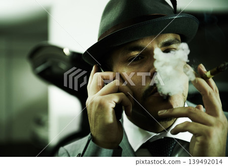 Man, gangster and phone call while smoking or planning mafia, danger or ransom abduction. Male person, cigar and mobile device or hitman conversation for robbery violence, interrogation or terror 139492014