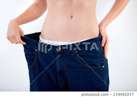 Weight, loss and abdomen of woman in jeans with comparison of size on white background in studio. Healthy, body and person with transformation or change from diet and show results in denim pants 139492037