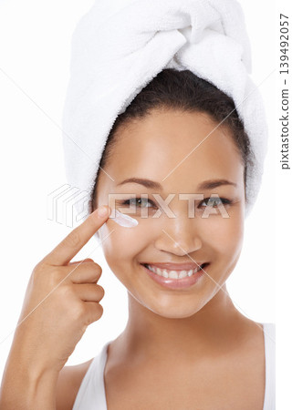 Happy woman, face and beauty cream, skincare and cosmetics on a white background. Portrait of an African model or person smile and apply moisturizer, lotion or eye product for dermatology in studio 139492057