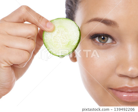 Skincare, cucumber and woman face or eye beauty for cosmetics, natural product and Vitamin C makeup in studio. Portrait of a young, happy model with green fruit and dermatology on a white background 139492206