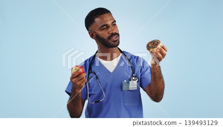 Doctor, man and studio for donut, apple and choice with thinking for healthcare by blue background. Medic, person or nutritionist with decision, cake and fruit with ideas for food, eating and diet Doctor, man and studio for donut, apple and choice with thinking for healthcare by blue background. Medic, person or nutritionist with decision, cake and fruit with ideas for food, eating and diet 139493129