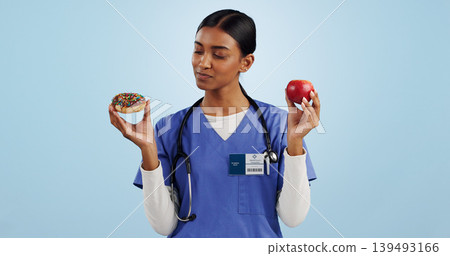 Apple, donut and doctor in studio with choice for healthy eating, diet and detox on blue background. Thinking, healthcare and Indian woman with candy, fruit and cake for decision, diabetes or balance 139493166