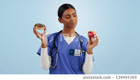 Apple, donut and nurse in studio with choice for healthy eating, diet and detox on blue background. Thinking, healthcare and Indian woman with dessert, fruit and cake for decision, option and balance 139493169