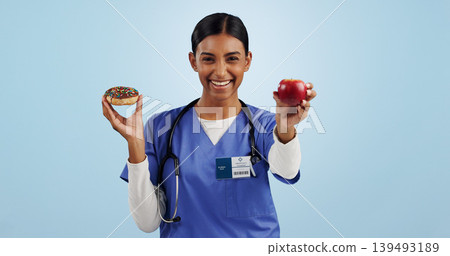 Apple, donut and portrait of nurse with choice for healthy eating, diet and detox on blue background. Happy, healthcare and Indian woman with dessert, fruit and cake for decision, options and balance Apple, donut and portrait of nurse with choice for healthy eating, diet and detox on blue background. Happy, healthcare and Indian woman with dessert, fruit and cake for decision, options and balance 139493189