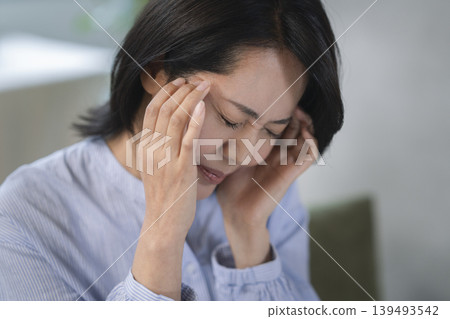 A woman in her 40s holds her temples with both hands. A woman in her 40s holds her temples with both hands. 139493542