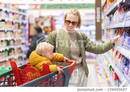 Caucasian mother shopping with her infant baby boy child choosing products in department of supermarket grocery store Caucasian mother shopping with her infant baby boy child choosing products in department of supermarket grocery store 139493687