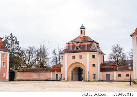 Wiblingen Abbey in Ulm, Germany features historic architecture with a large archway and two buildings. The scene is set against a cloudy sky. 139493815