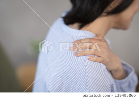 A middle-aged woman's hand resting on her shoulder while she is sitting. A middle-aged woman's hand resting on her shoulder while she is sitting. 139493860