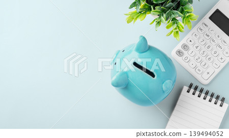 Top view of blue piggy bank with calculator and spiral notebook on blue background, finance planning, personal savings, and budgeting 139494052