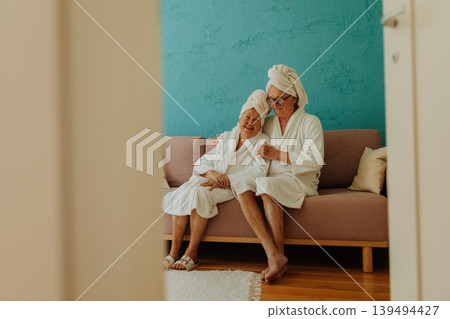 Portrait of happy senior couple sitting together in bathrobe on sofa. 139494427