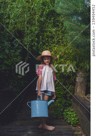 Little girl holding watering can in lush garden pathway. Little girl holding watering can in lush garden pathway. 139494452