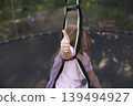 Happy excited child girl sitting on trampoline outdoor showing thumb up sign 139494927