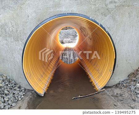 A large corrugated plastic drainage pipe is seen from inside, integrated into a concrete wall. This structure is part of infrastructure and sewage system work. Water flows through the pipe opening. 139495275