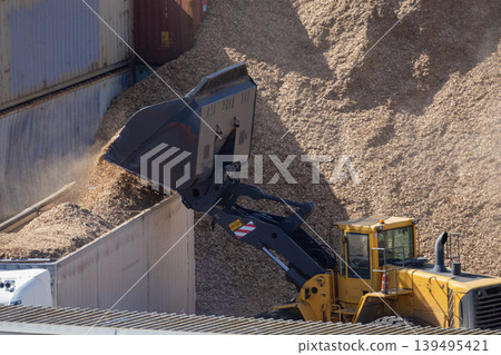 Large machine moves wood chips at a storage site in the afternoon sun during a busy workday Large machine moves wood chips at a storage site in the afternoon sun during a busy workday 139495421