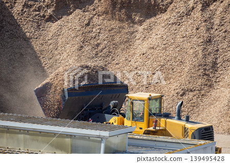 Heavy machinery moves wood chips at a lumber yard in the afternoon under clear skies Heavy machinery moves wood chips at a lumber yard in the afternoon under clear skies 139495428