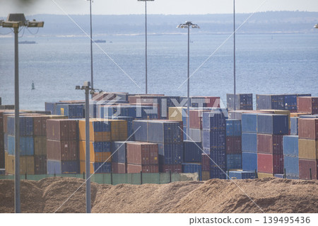 Cargo containers stacked near the waterfront in a busy port during daylight hours Cargo containers stacked near the waterfront in a busy port during daylight hours 139495436