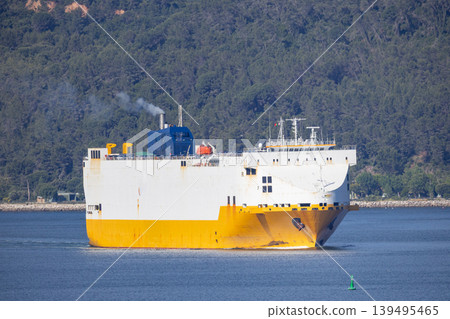 Cargo ship moves through water near coastline while smoke rises from its stack in the distance 139495465