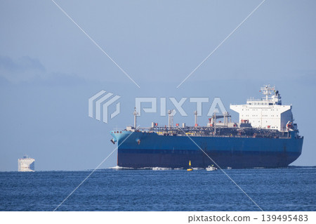 Large cargo ship navigates near small vessel in open water on clear day 139495483