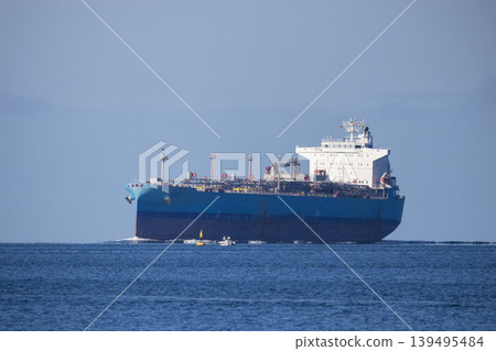 Large cargo ship transports goods across the open sea near a coastal area during bright daylight hours Large cargo ship transports goods across the open sea near a coastal area during bright daylight hours 139495484